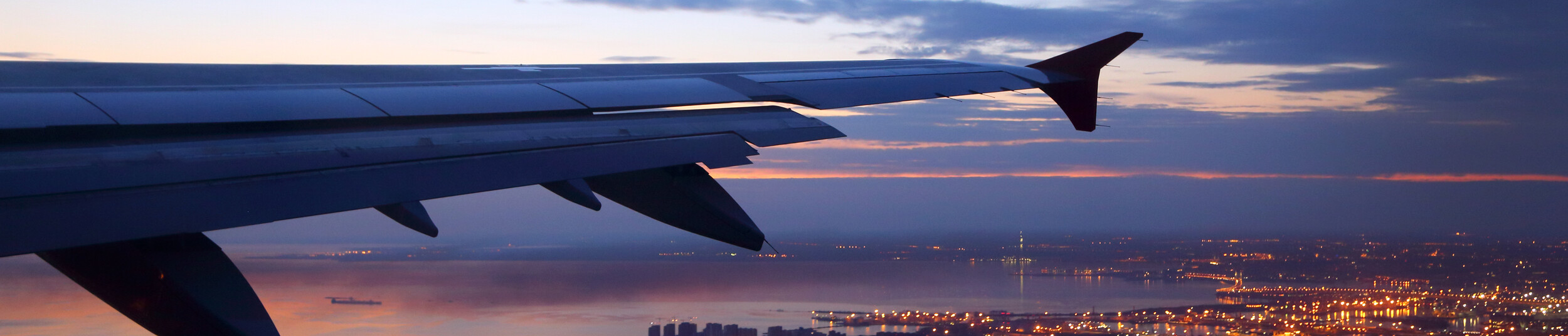 a photo showing the wing of a plane flying at night along the skyline